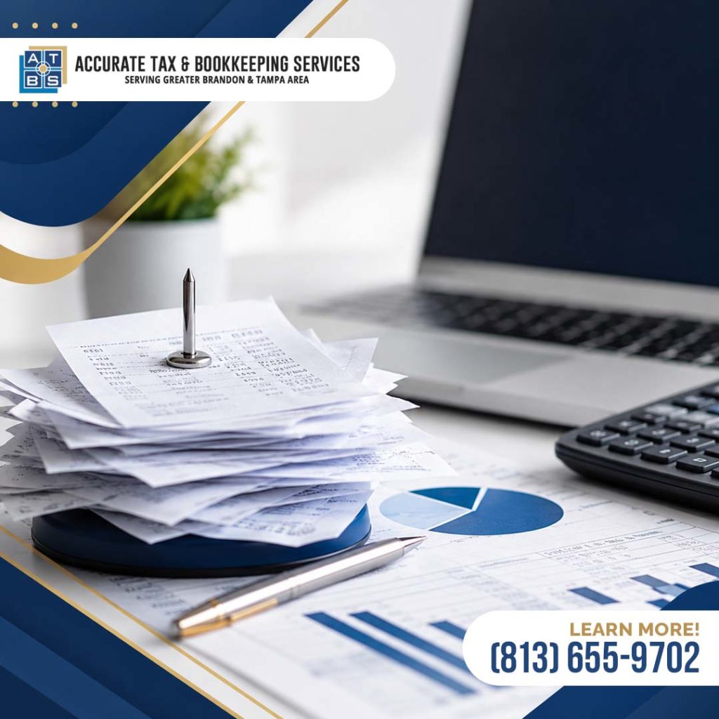 A stack of paper business receipts held on a metal receipt spindle next to financial documents, a laptop, and a calculator on an office desk.